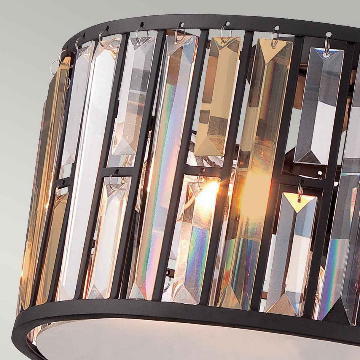 Close-up of the Gemma 3 Light Flush in Vintage Bronze, featuring vertical, multicolored crystal prisms. The prisms catch light from the bulb inside, creating shimmering reflections.
