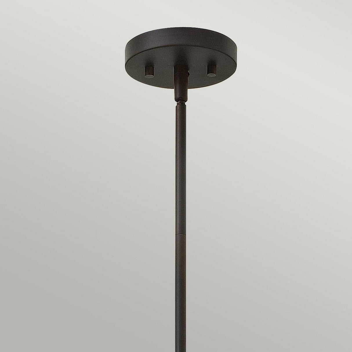 The Gemma 1 Light Mini Pendant in vintage bronze showcases a minimalist design with a black cylindrical ceiling mount and a straight rod, enhanced by vintage bronze accents against a simple gray background.