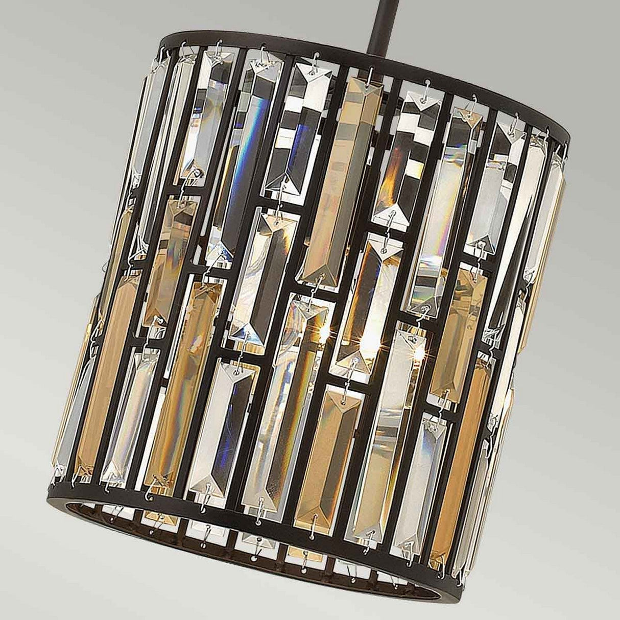 The Gemma 1 Light Mini Pendant in Vintage Bronze features a close-up view of decorative vertical rows of rectangular, translucent glass prisms within its frame, reflecting light to create stunning geometric patterns.