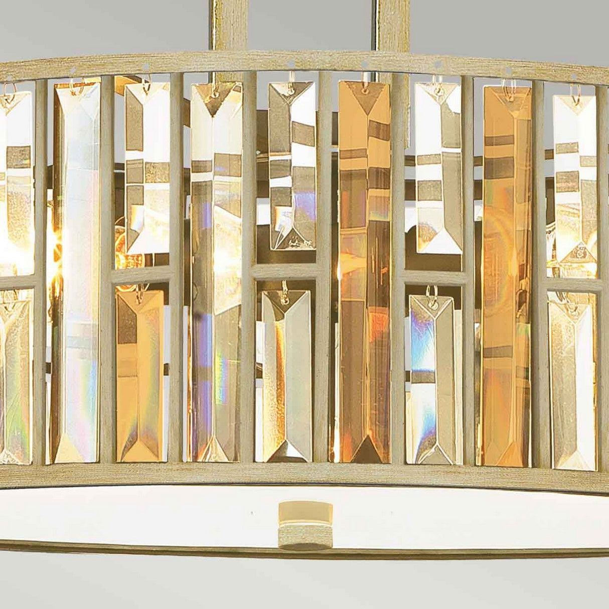 A close-up of the Gemma 3 Light Chandelier - Gold reveals vertical rectangular crystals in shades of gold and clear. These elegant crystals reflect light, creating a shimmering effect. The base of the fixture boasts a soft metallic hue, enhancing its luxurious appeal.