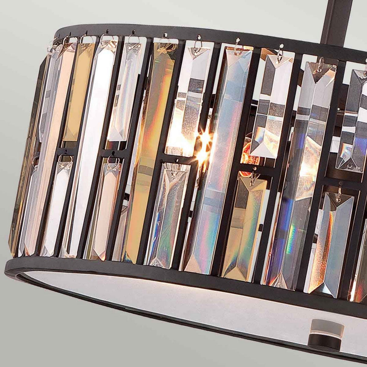 A close-up showcases the Gemma 3 Light Chandelier, featuring rectangular, prism-like crystals mounted on a black circular frame with vintage bronze accents. The crystals beautifully reflect rainbow colors in a contemporary style against a neutral background.