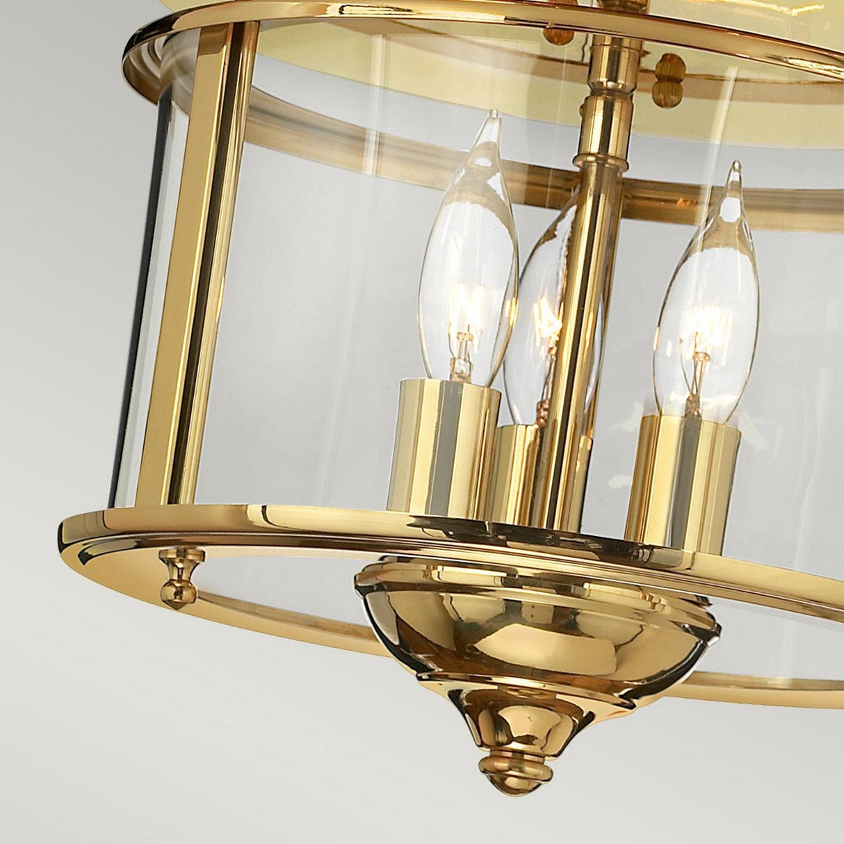Close-up of the Gentry 3 Light Flush - Polished Brass, a traditional gold ceiling light fixture featuring clear glass panels and three candle-like bulbs, elegantly designed to reflect light beautifully.