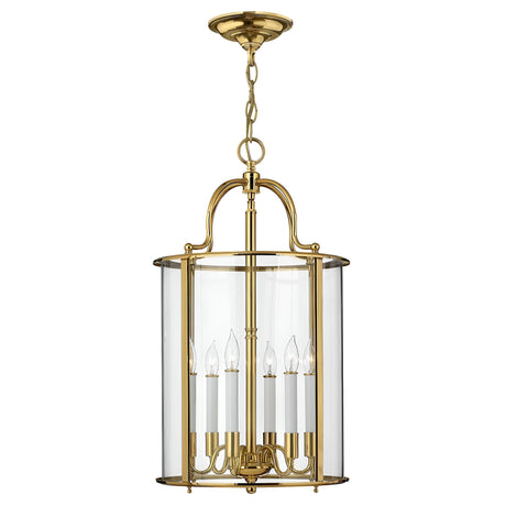 The Gentry 6 Light Large Pendant in polished brass features a traditional design, showcasing clear bent glass within its cylindrical casing. It includes six candle-shaped light fixtures and a decorative chain for hanging.