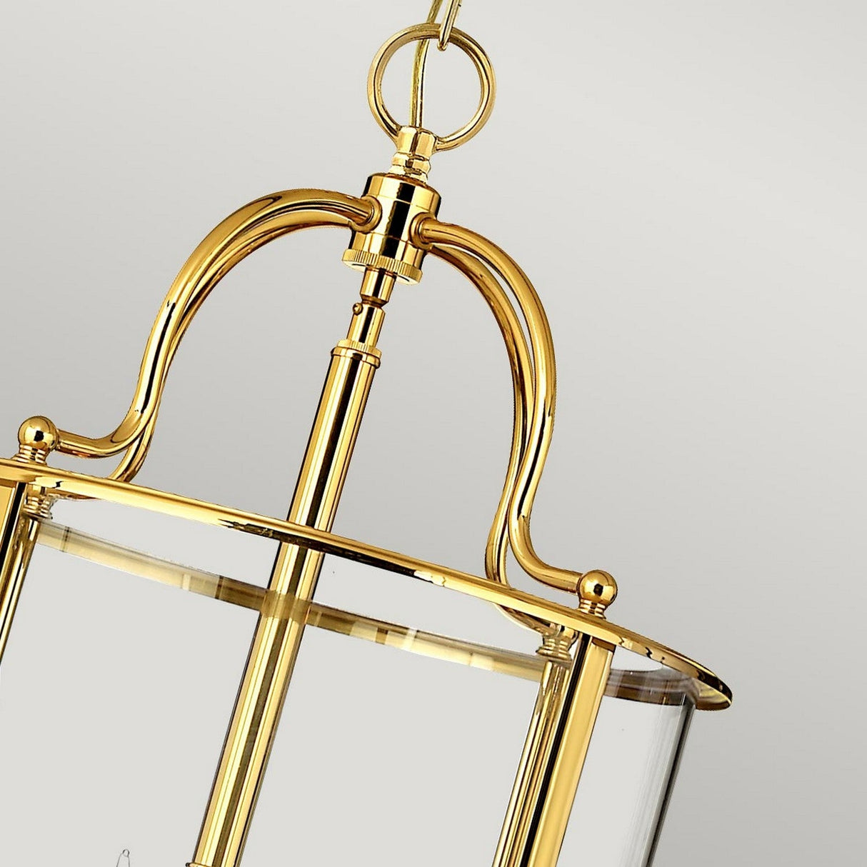 A close-up of the Gentry 6 Light Large Pendant in polished brass showcases its elegant lantern-style design. It features clear bent glass and curved metalwork, complete with a round top handle, set against a neutral gray background. This sophisticated piece adds a touch of traditional design to any setting.