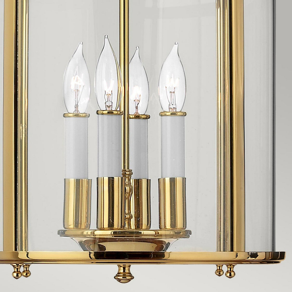 Close-up of the Gentry 4 Light Medium Pendant in polished brass, showcasing its elegant design with four candle-style light bulbs encased in clear bent glass panels. The traditional piece features classic, ornate detailing and a reflective finish.