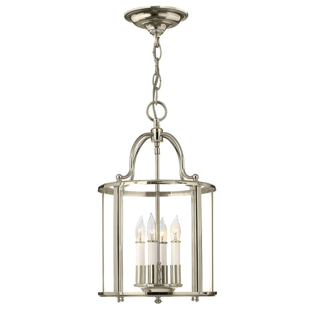 The Gentry 4 Light Medium Pendant in polished nickel hangs gracefully from a chain, showcasing a chic lantern design. Its clear glass panels encase four candle-shaped bulbs, offering an elegant and modern lighting fixture.