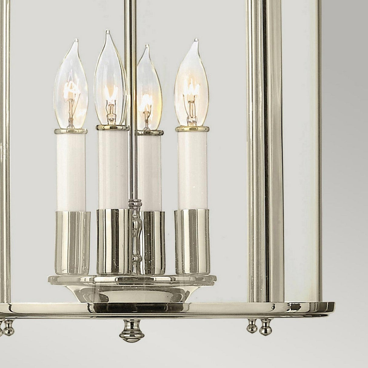 A close-up of the Gentry 4 Light Medium Pendant - Polished Nickel reveals a modern lighting fixture with four candle-shaped bulbs featuring flame-shaped tips, elegantly encased in a cylindrical glass cover within its polished nickel frame.