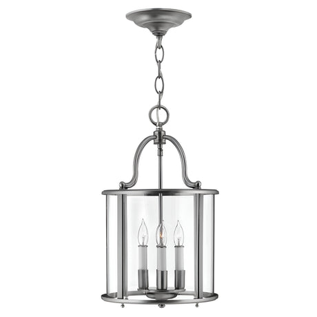 The Gentry 4 Light Medium Pendant - Silver features a brushed metal finish and clear bent glass panels. Inside, four candle-style sockets hold clear bulbs, all elegantly encased. Suspended by a chain, this sophisticated silver pendant showcases a gracefully curved design that exudes timeless elegance.