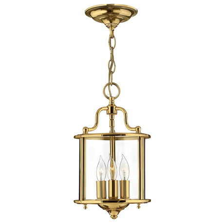 The Gentry 3 Light Small Pendant in polished brass showcases a chain attachment and three candle-shaped light bulbs encased in clear glass. This elegant and classic design embodies traditional lighting style, making it ideal for enhancing any classic interior.