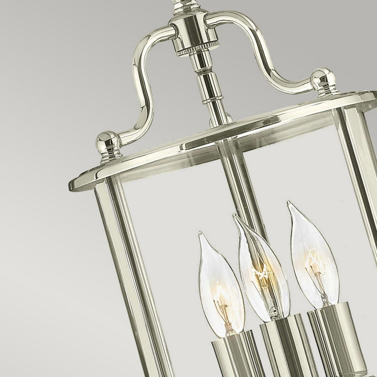 A detailed view of the Gentry 3 Light Small Pendant in polished nickel showcases an elegant and modern design. The fixture features several candle-shaped light bulbs encased within clear bent glass, offering a sophisticated and contemporary aesthetic against a simple gray backdrop.