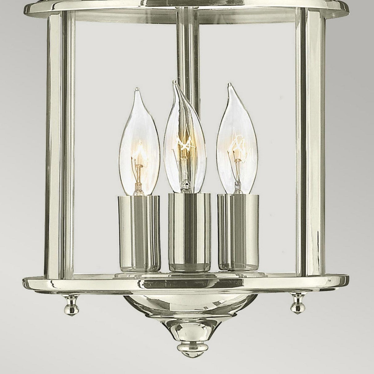 The Gentry 3 Light Small Pendant in polished nickel features an elegant design with three candle-shaped light bulbs enclosed in a clear bent glass frame. This classic fixture is ideal for indoor lighting, adding charm to any space.