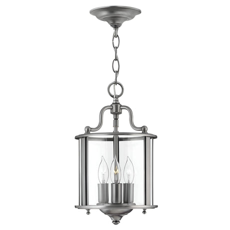 The Gentry 3 Light Small Pendant - Silver is a hanging lantern-style fixture with a sleek silver finish. It features three candle-shaped bulbs elegantly enclosed in clear bent glass panels, all suspended from the ceiling by a chain.