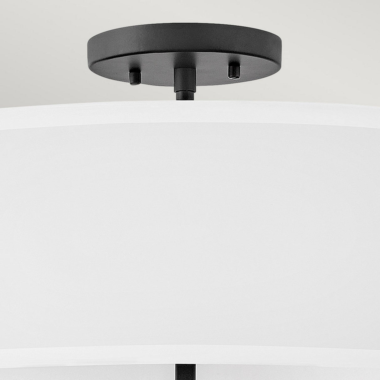 A close-up of a modern ceiling light fixture showcases the Graham 4 Light Duo-Mount Pendant/Semi-Flush in Black, featuring a sleek black metal base and a large white fabric lampshade that exudes classic charm. It is elegantly installed on a light grey ceiling.