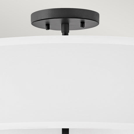 A close-up of a modern ceiling light fixture showcases the Graham 4 Light Duo-Mount Pendant/Semi-Flush in Black, featuring a sleek black metal base and a large white fabric lampshade that exudes classic charm. It is elegantly installed on a light grey ceiling.