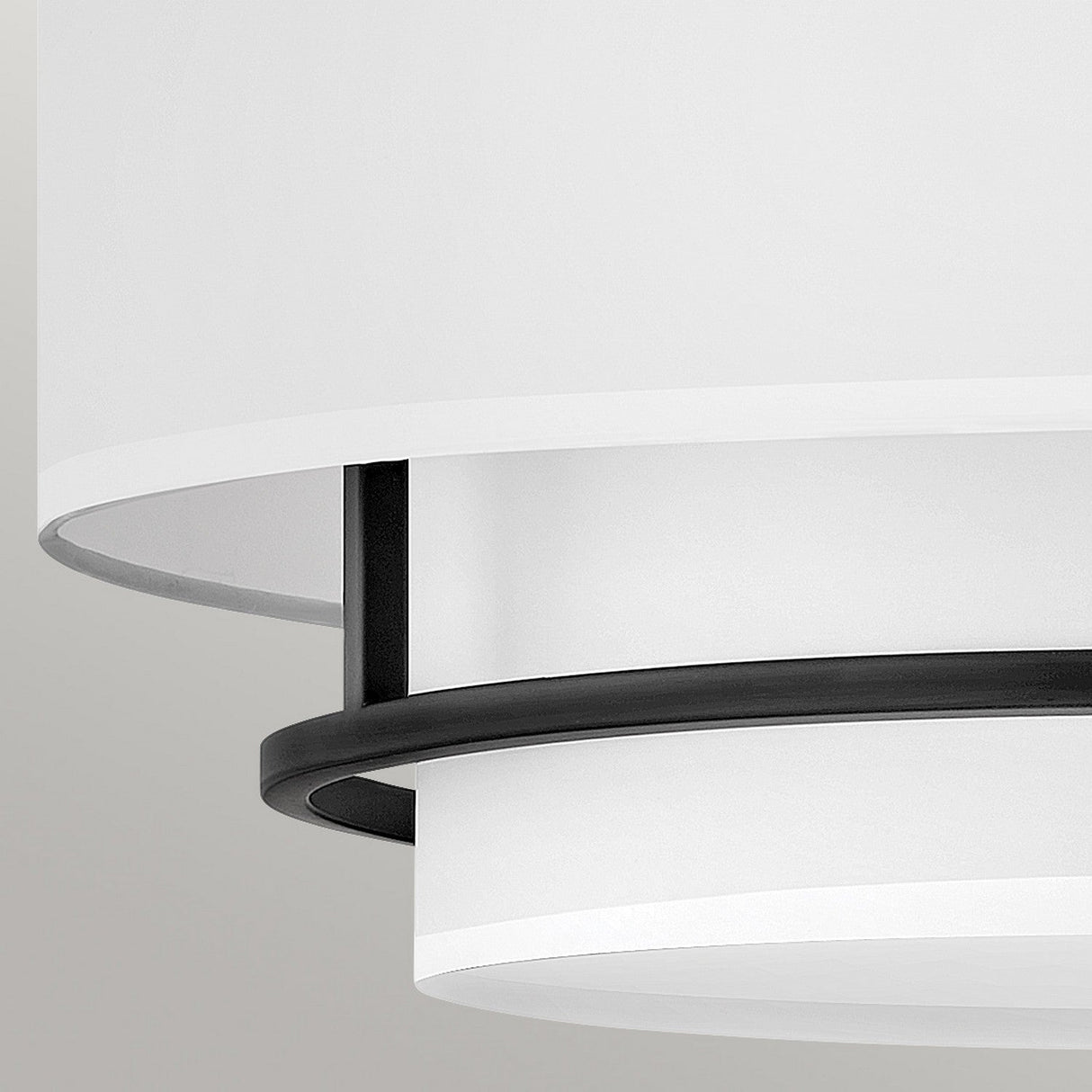 A close-up of the Graham 4 Light Duo-Mount Pendant/Semi-Flush in black showcases its modern, circular design with a minimalist aesthetic. The fixture exudes classic charm with a white drum shade accented by a black metal ring. The light gray background complements the sleek appearance of this fixture.