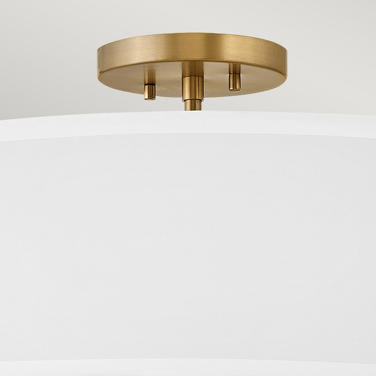 A close-up of the Graham 4 Light Duo-Mount Pendant/Semi-Flush reveals a white cylindrical shade accompanied by lacquered brass mounting. Its minimalist design radiates modern elegance, seamlessly enhancing the neutral background while capturing the sophisticated style of this lighting fixture.