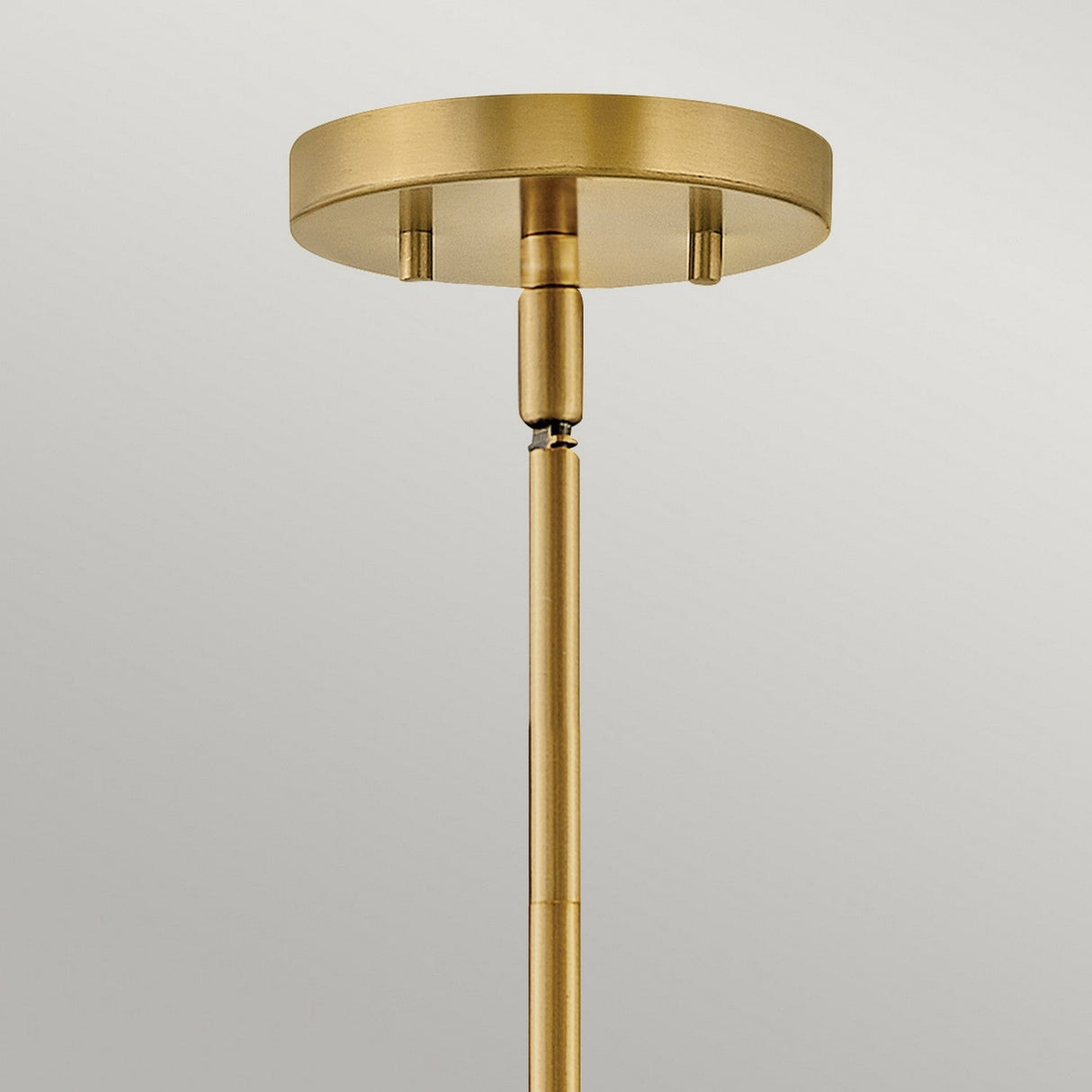 Close-up of the sleek, modern Graham 4 Light Duo-Mount Pendant/Semi-Flush in lacquered brass, featuring a minimalist design with a cylindrical rod and round base. It casts a warm golden hue and is set against a plain, light gray background.