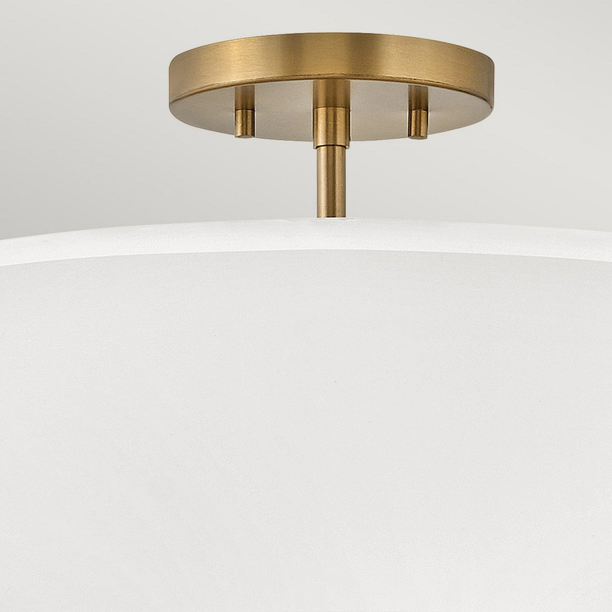 Close-up of a modern ceiling light fixture showcasing the Graham 3 Light Duo-Mount Pendant/Semi-Flush in lacquered brass, featuring a round mount and a white curved shade. Its neutral colors and minimalist design project a contemporary aesthetic while providing dual-mount functionality.