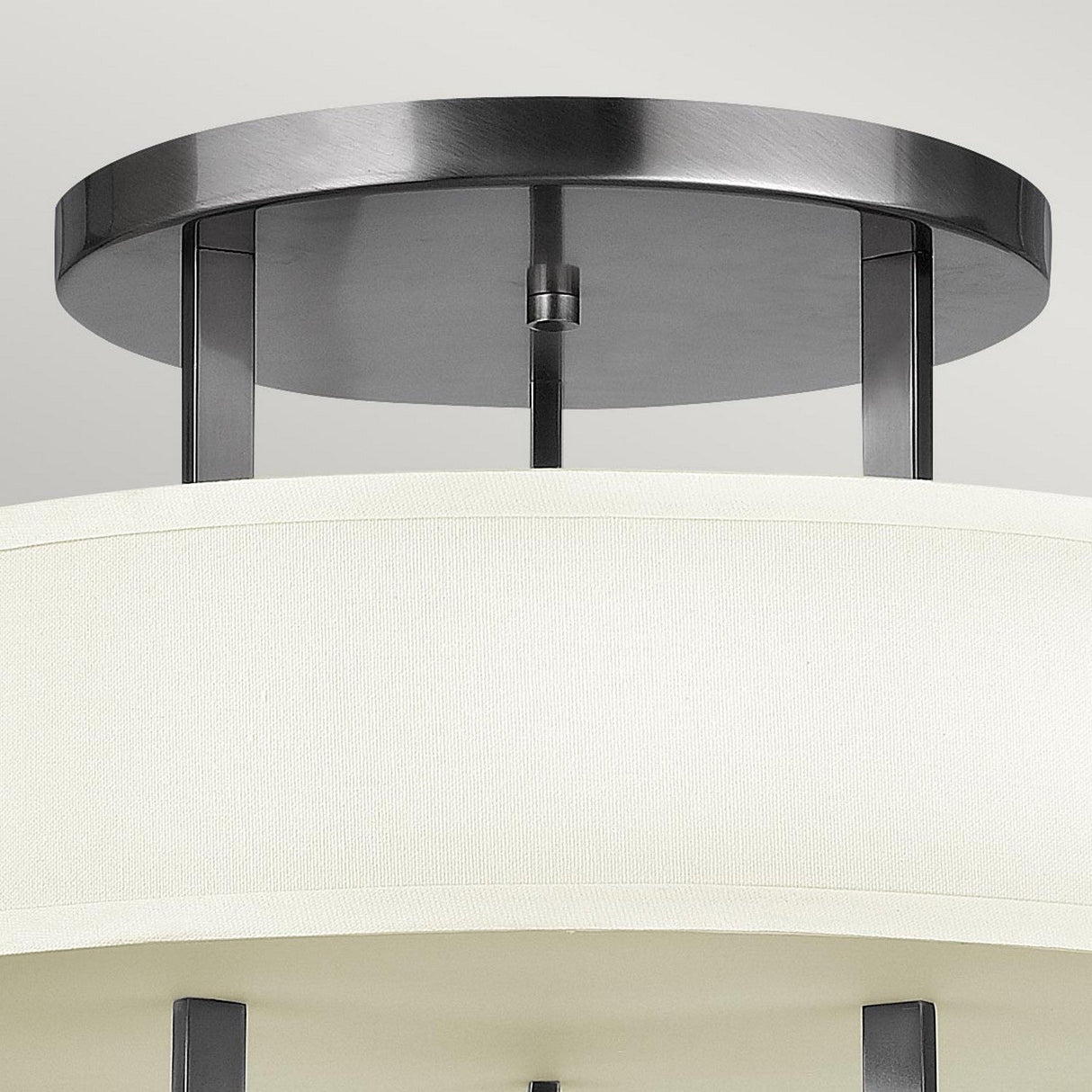 Close-up of a Hampton 3 Light Semi Flush ceiling fixture, featuring a circular metal base and an ivory drum shade. The elegant metal supports in an Antique Nickel finish enhance its contemporary appearance.