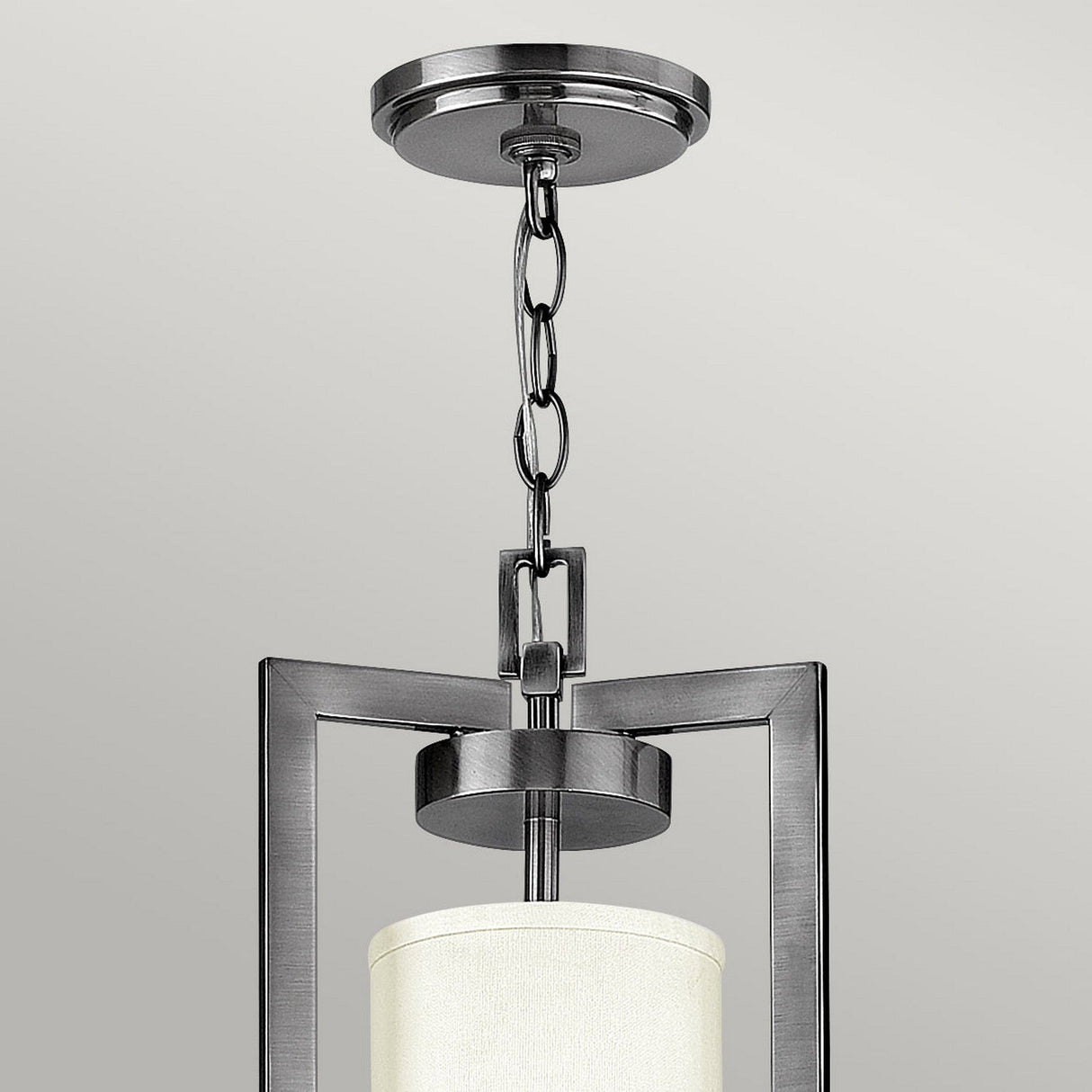 The Hampton 4 Light Chandelier, featuring an Antique Nickel finish and an Ivory shade, showcases a modern pendant design with a brushed metal frame and cylindrical lampshade. Its sleek look is reminiscent of Transitional Design, as it hangs elegantly from a chain attached to a ceiling mount.