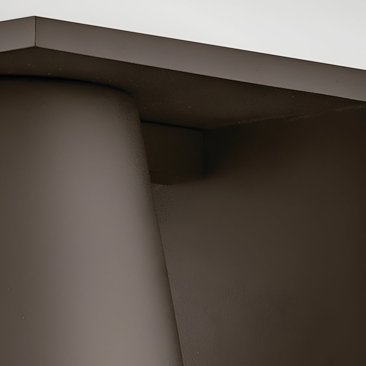 Close-up of the Coastal 1 Light Small Outdoor Wall Lantern in architectural bronze, featuring a smooth matte brown surface with curved and angled edges under soft lighting.