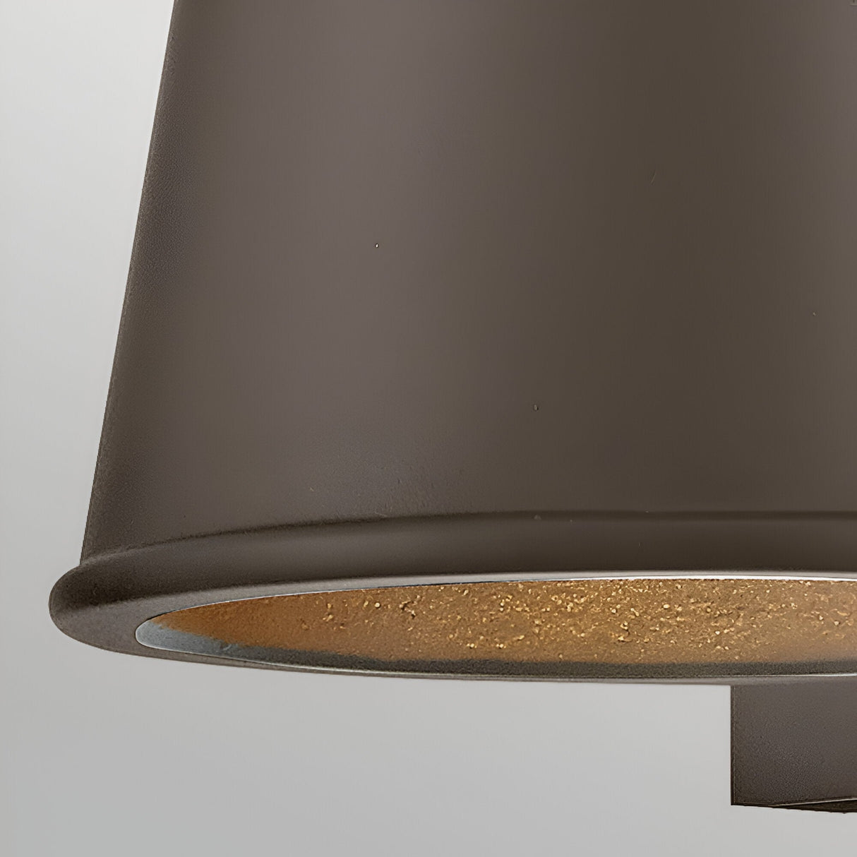 Close-up of the Coastal 1 Light Small Outdoor Wall Lantern in architectural bronze, showing its textured golden interior. This weather-resistant fixture is partially visible against a plain light background.