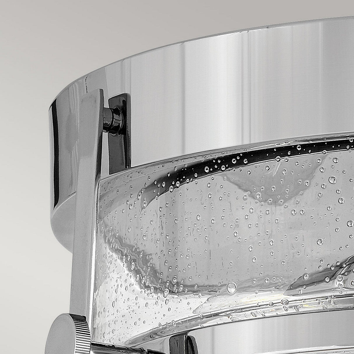 A close-up image features the Harper 3 Light Flush, showcasing its modern transparent glass container with a polished chrome band. The clear liquid and bubbles within highlight the design's elegance. The neutral light gray background emphasizes the sleek, reflective nature of its materials, drawing attention to the clear seeded glass detailing.