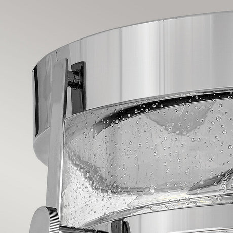 A close-up image features the Harper 3 Light Flush, showcasing its modern transparent glass container with a polished chrome band. The clear liquid and bubbles within highlight the design's elegance. The neutral light gray background emphasizes the sleek, reflective nature of its materials, drawing attention to the clear seeded glass detailing.