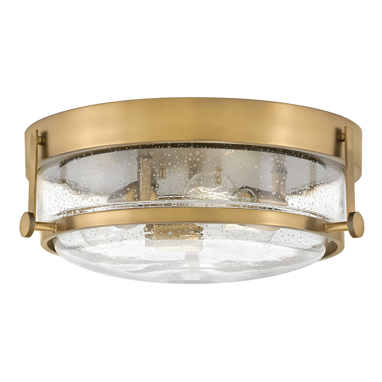Introducing the Harper 3 Light Flush fixture, featuring a Heritage Brass frame and clear seeded glass. The bubble-textured glass showcases visible bulbs, creating a sleek design that elegantly merges modern and retro elements.