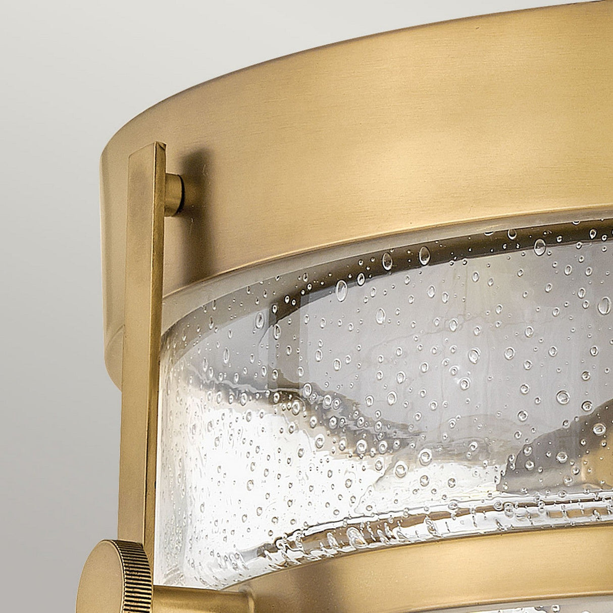 A close-up of the Harper 3 Light Flush showcases its heritage brass frame and clear seeded glass shade. The bubble-like textures of the glass give it a retro design, blending sophistication and modern elegance against a soft, neutral background.