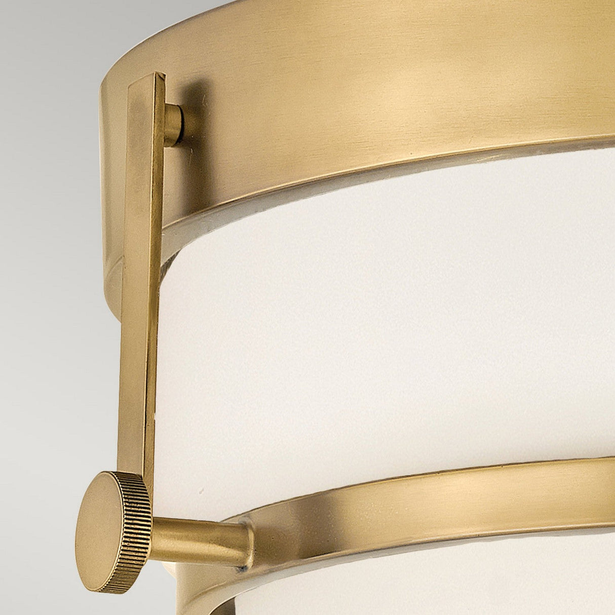 A close-up of the Harper 3 Light Flush showcases its modern cylindrical design in a heritage brass finish. This fixture features two horizontal support elements and is complemented by an opal etched glass shade, achieving a sleek and sophisticated aesthetic reminiscent of flush mount lighting.