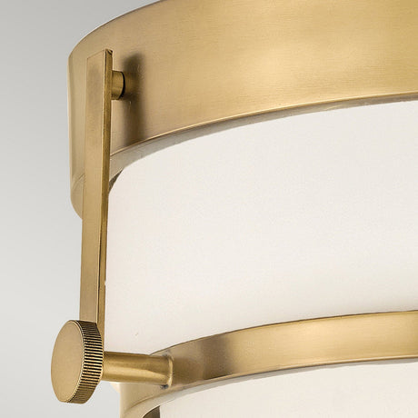 A close-up of the Harper 3 Light Flush showcases its modern cylindrical design in a heritage brass finish. This fixture features two horizontal support elements and is complemented by an opal etched glass shade, achieving a sleek and sophisticated aesthetic reminiscent of flush mount lighting.
