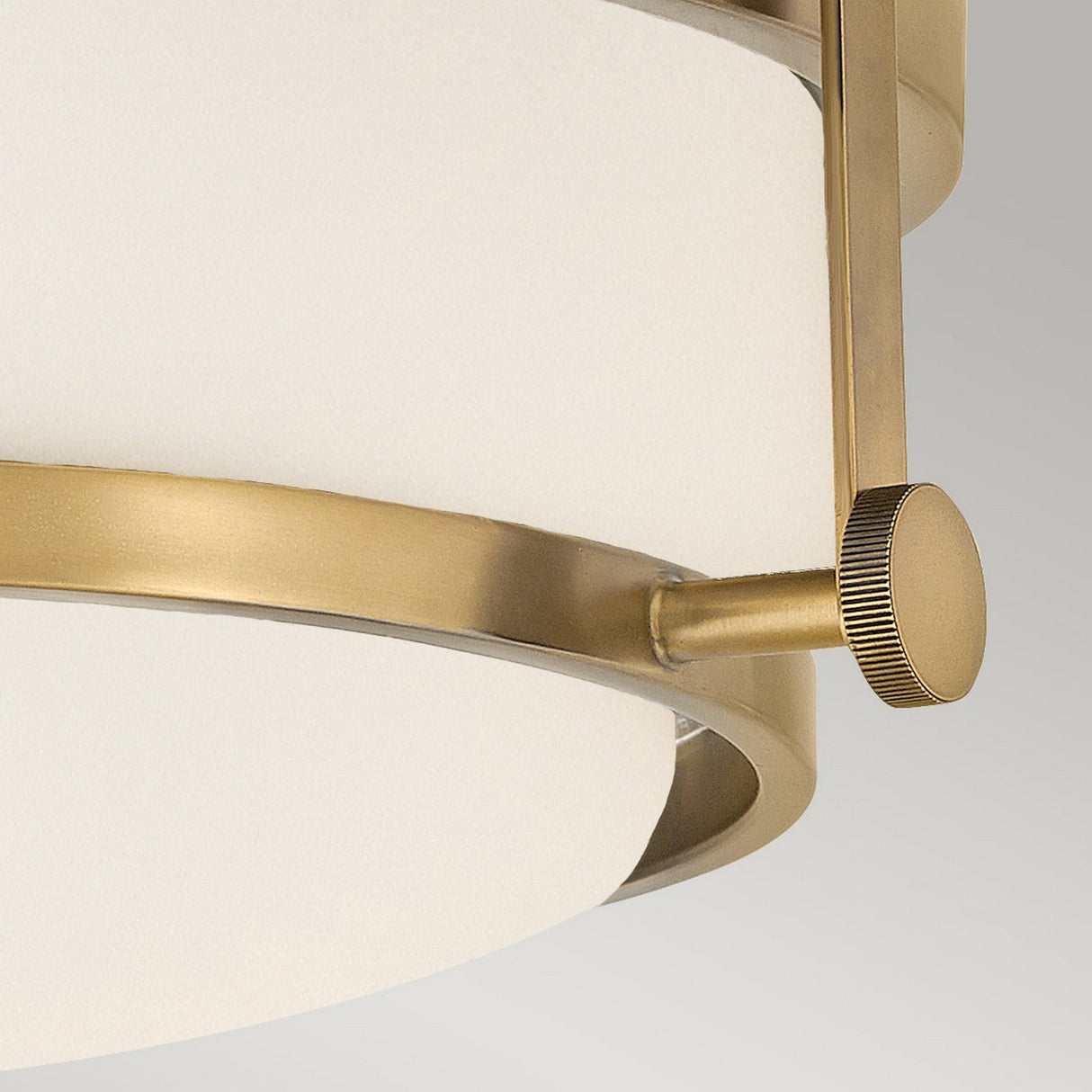 Close-up of the Harper 3 Light Flush, featuring a circular design with an opal etched glass shade. This modern ceiling light fixture, reminiscent of Heritage Brass, showcases a brushed brass metal frame with knurled knob detail, elegantly set against a plain gray background.