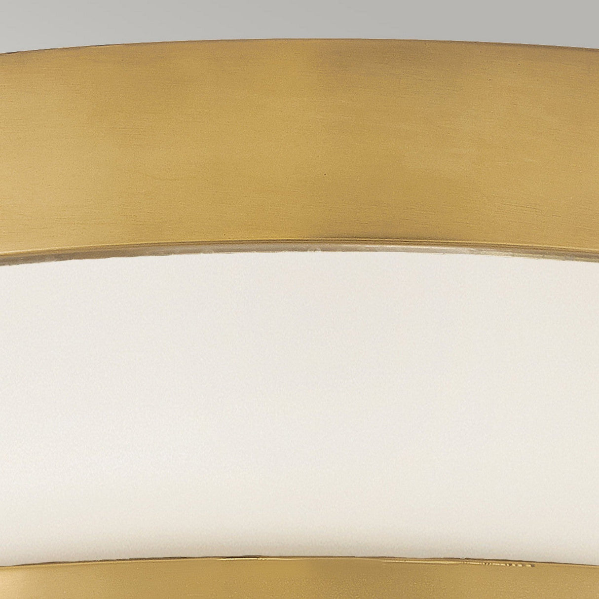 A close-up of the Harper 3 Light Flush in heritage brass and opal etched glass, showcasing its elegant curved design against a gray background, which suggests it is part of a decorative item or furniture piece.