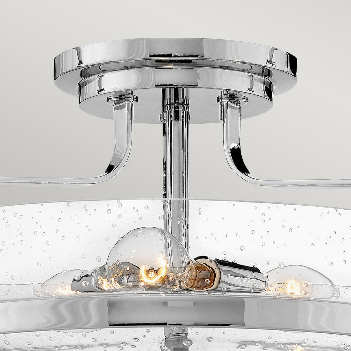 Close-up of the Harper 3 Light Medium Semi Flush, boasting a polished chrome finish. It highlights clear seeded glass shades with a bubbled texture that reveal the bulbs inside, and features two curved metal arms attaching it to the ceiling.