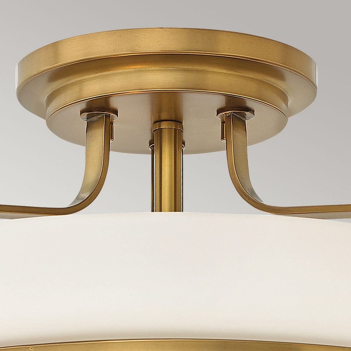 Close-up of the Harper 3 Light Medium Semi Flush in Heritage Brass, showcasing its circular mount and elegantly curved supports. The fixture features an opal etched glass shade, delivering a sophisticated and timeless appearance against a neutral background.