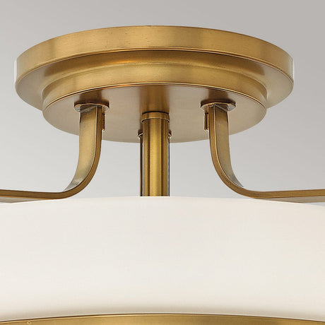 Close-up of the Harper 3 Light Medium Semi Flush in Heritage Brass, showcasing its circular mount and elegantly curved supports. The fixture features an opal etched glass shade, delivering a sophisticated and timeless appearance against a neutral background.