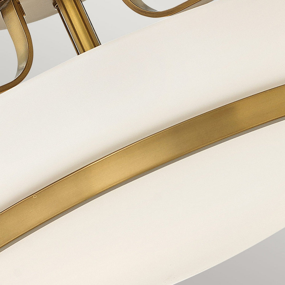A detailed view of the Harper 3 Light Medium Semi Flush reveals its opal etched glass featuring a graceful curved design. The heritage brass components encircle the white section, offering a contemporary and sophisticated look against a neutral setting.