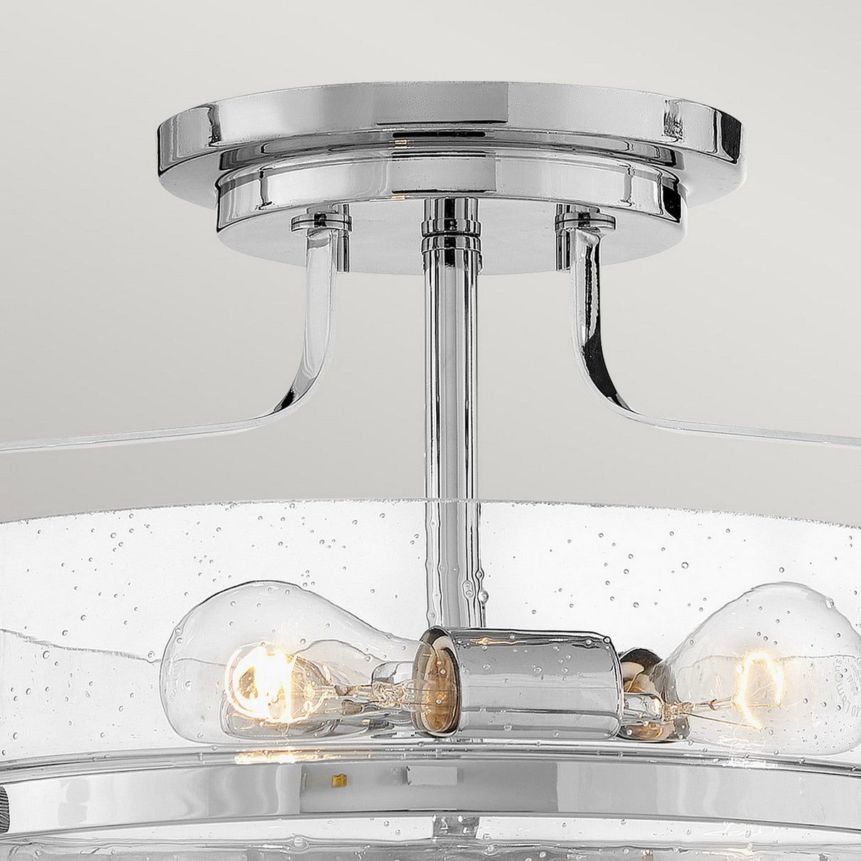 Close-up of the Harper 3 Light Small Semi Flush featuring a polished chrome round base and three filament bulbs. This modern ceiling light fixture includes a clear seeded glass shade with small bubbles, resulting in an elegant and contemporary appearance.