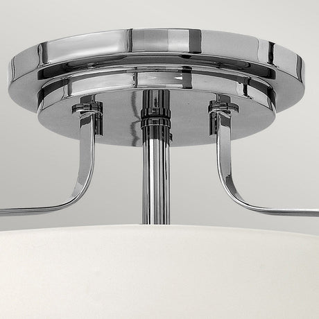 A close-up of the Harper 3 Light Small Semi Flush fixture showcases its polished chrome finish and modern design. Featuring a circular base with elegantly curved supports attached to the main frame, this stylish piece reflects light beautifully against a neutral background, enhanced by opal etched glass.