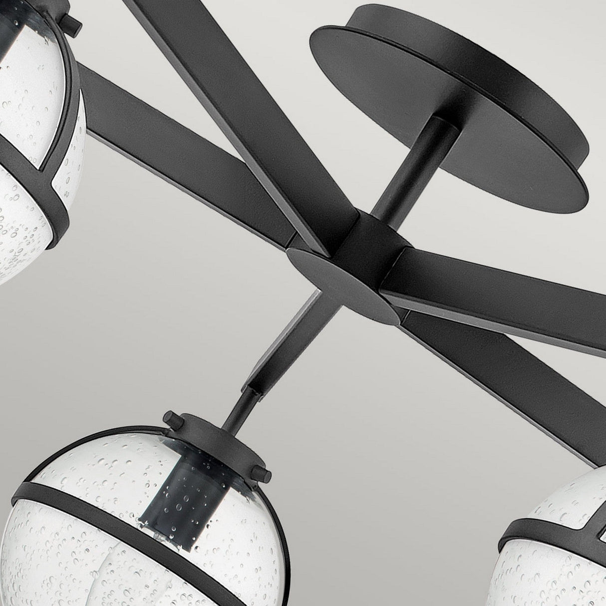 Close-up of the Hollis 5 Light Semi Flush fixture in black, showcasing its sleek metal frame. This light features a Mid-Century Modern design with round, clear seeded glass globes that have a speckled texture, elegantly encasing the bulbs against a light gray background.