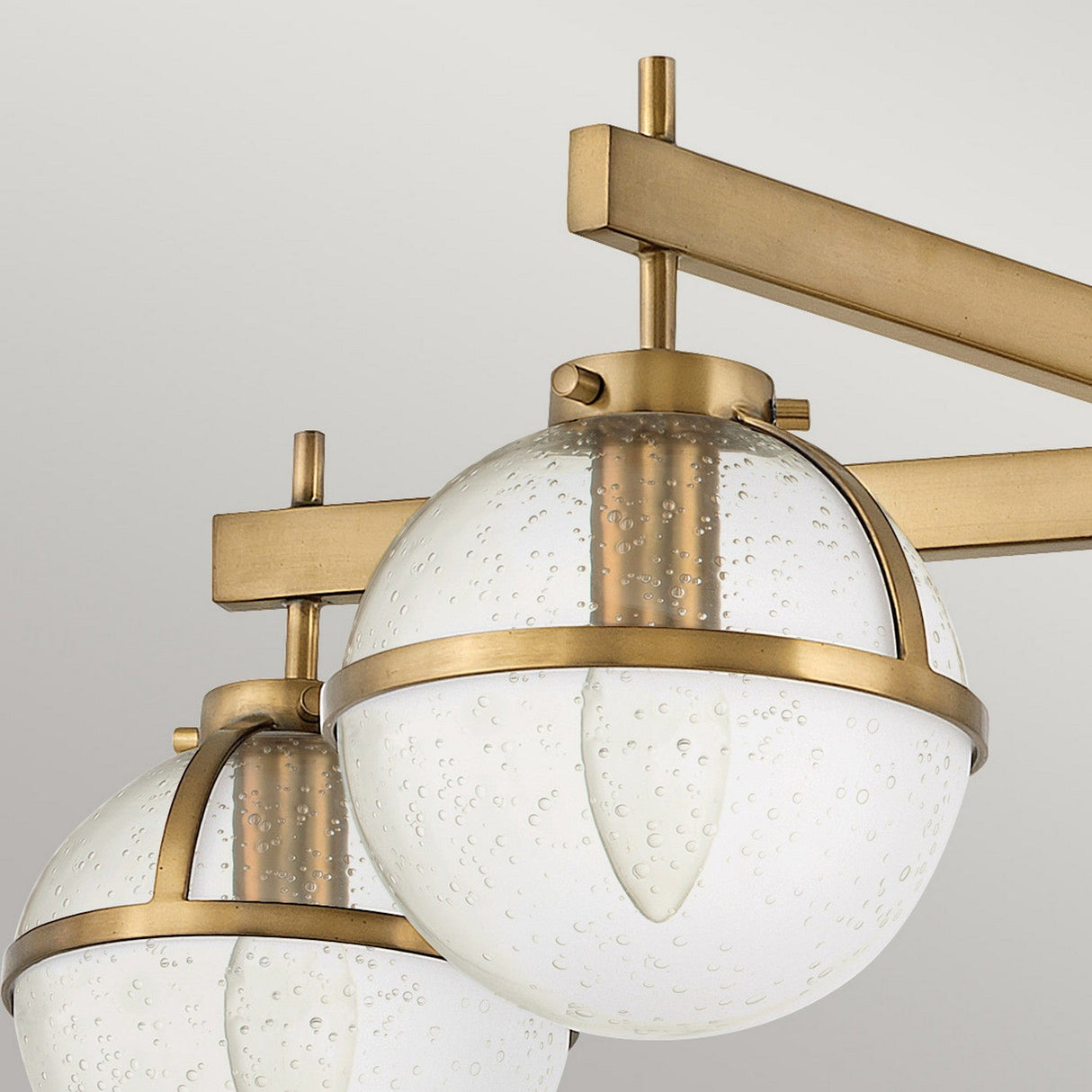 Close-up of a contemporary light fixture showcasing clear seeded glass globes encased in a Heritage Brass frame. The design is minimalist and elegant, with a brushed gold finish on the supporting structure, exemplifying the Hollis 5 Light Semi Flush.