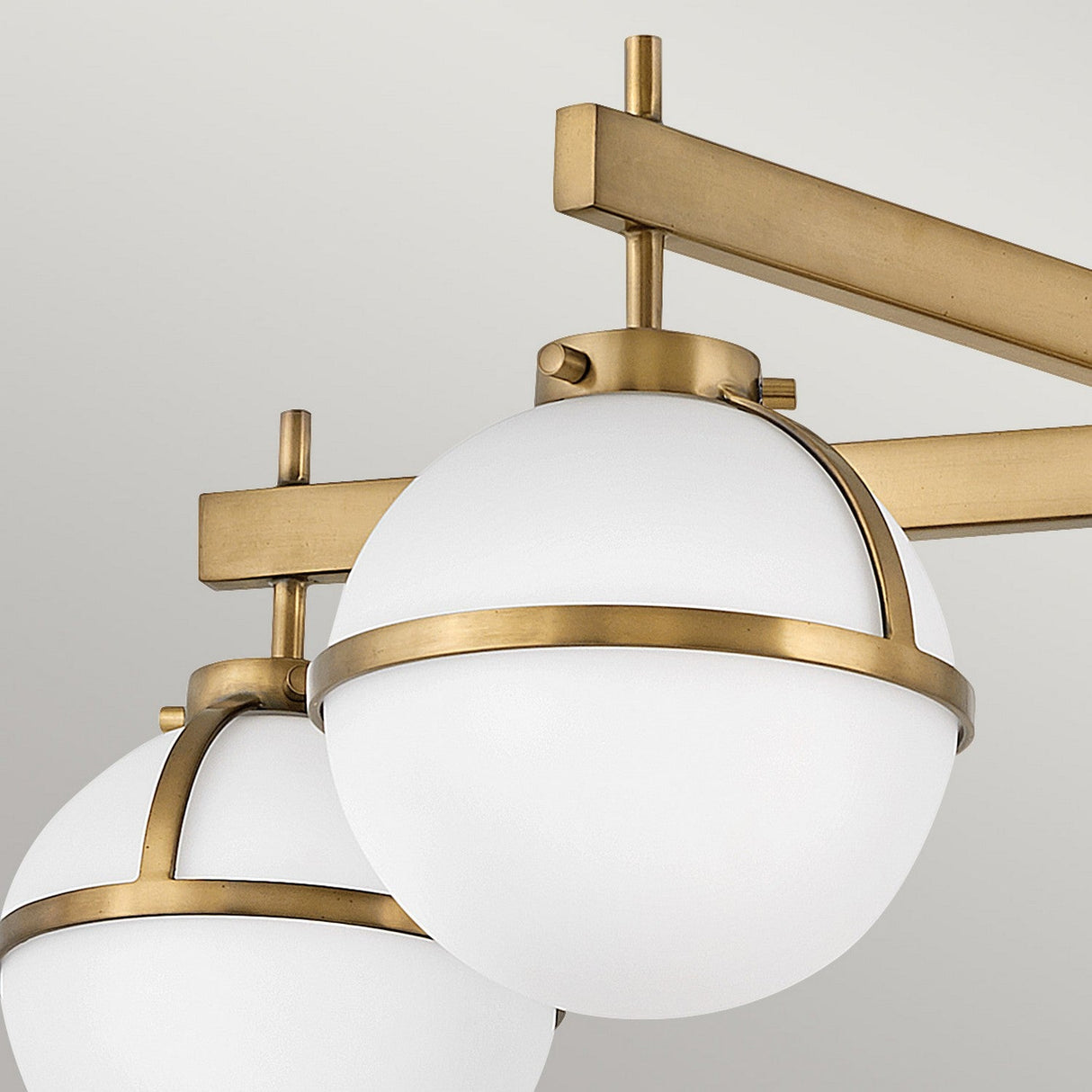 Close-up of the Hollis 5 Light Semi Flush with opal etched glass lampshades and heritage brass accents. The geometric design showcases intersecting metal rods, offering an elegant and contemporary appearance against a neutral background.