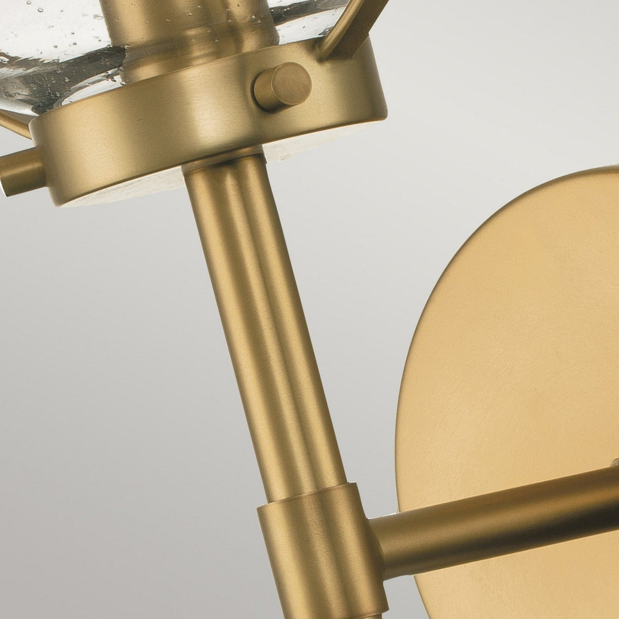 Close-up of the Hollis 1 Light Wall Light, a modern brass sconce featuring a cylindrical rod and circular backplate. This fixture echoes Art Deco elegance with its clear glass shade, presenting a sleek and contemporary design in heritage brass.