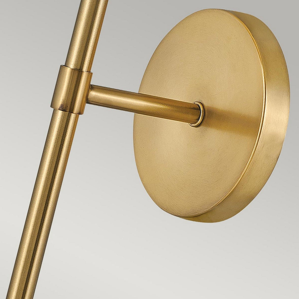 A detailed view of the Hollis 1 Light Wall Light in Heritage Brass reveals its round base and cylindrical arm, embodying Art Deco sophistication. The matte finish perfectly complements the opal glass shade, all set against a light gray gradient.