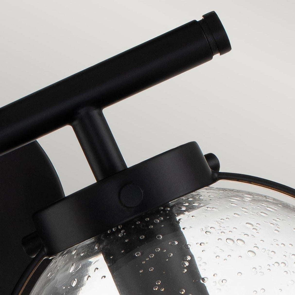 A close-up of the Hollis 2 Light Wall Light showcases its modern black finish paired with clear glass. The sleek, minimalist design is enhanced by the decorative bubble-textured surface, subtly echoing Art Deco lighting aesthetics.