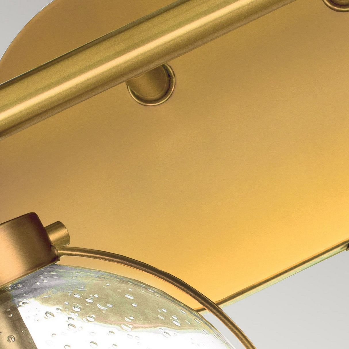 Close-up of the Hollis 2 Light Wall Light, featuring a modern Heritage Brass frame and a clear glass shade with delicate bubble details. Its contemporary circular design and intersecting elements bring elegance to any room.