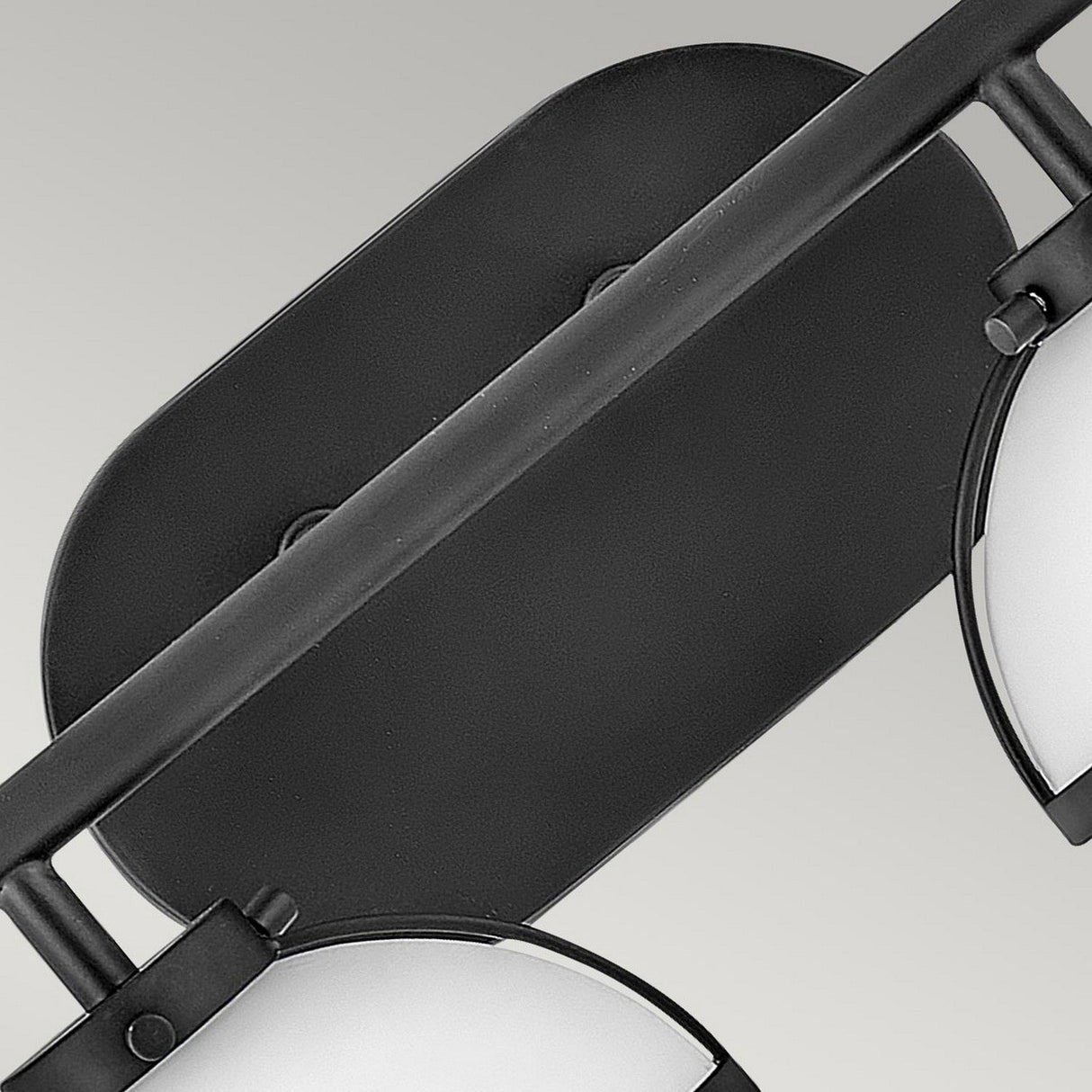 A close-up of the "Hollis 2 Light Wall Light" in a black finish showcases its oval shape with two partially visible round, frosted opal glass shades on each side, set against a plain, light gray background.