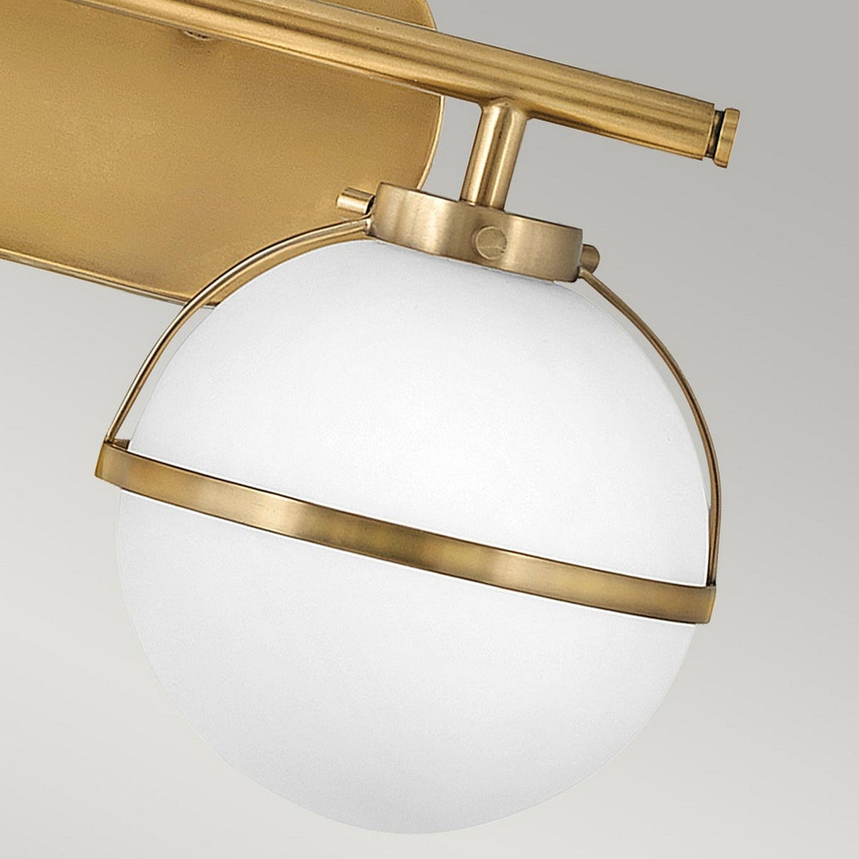 Close-up of the Hollis 2 Light Wall Light - Heritage Brass With Opal Glass, showcasing an opal glass globe within a heritage brass metallic frame, mounted on a coordinating gold mounting plate against a neutral gray background.