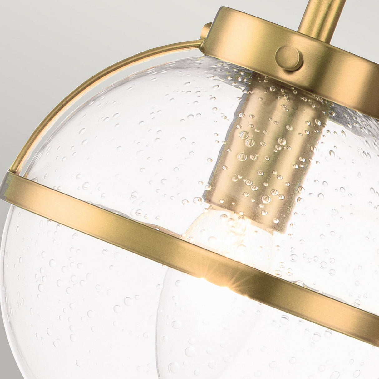 Close-up of the Hollis 3 Light Wall Light featuring Heritage Brass accents and clear glass with small bubbles throughout. The illuminated bulb inside casts a warm Art Deco glow.